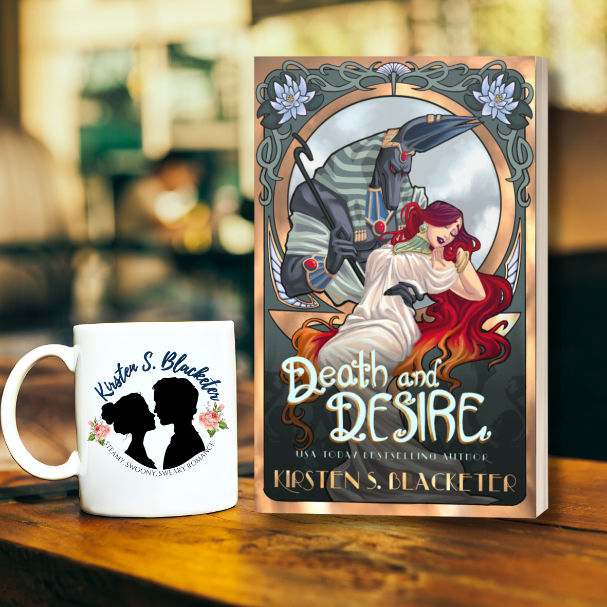 Paperback book "Death and Desire" with art nouveau floral frame and a woman with red hair being held by Anubis, Egyptian god of the dead. 