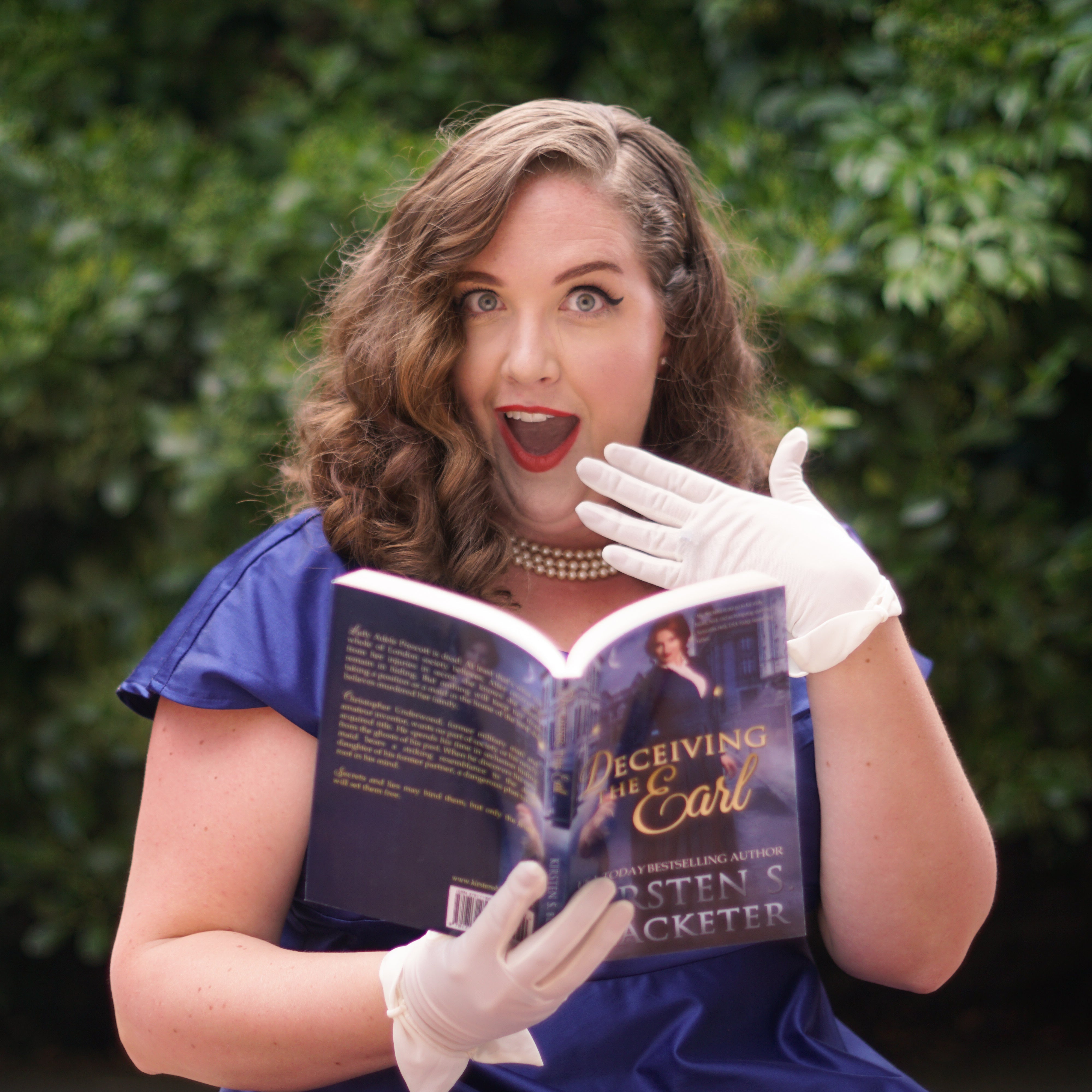 Woman in a blue dress and white gloves holding an open book with a green leafy background